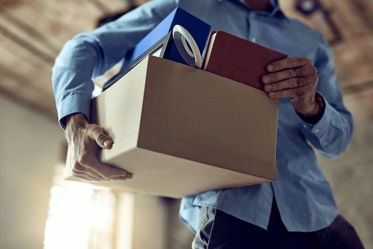 Imagem de um homem segurando uma caixa com seus pertences, após demissão.