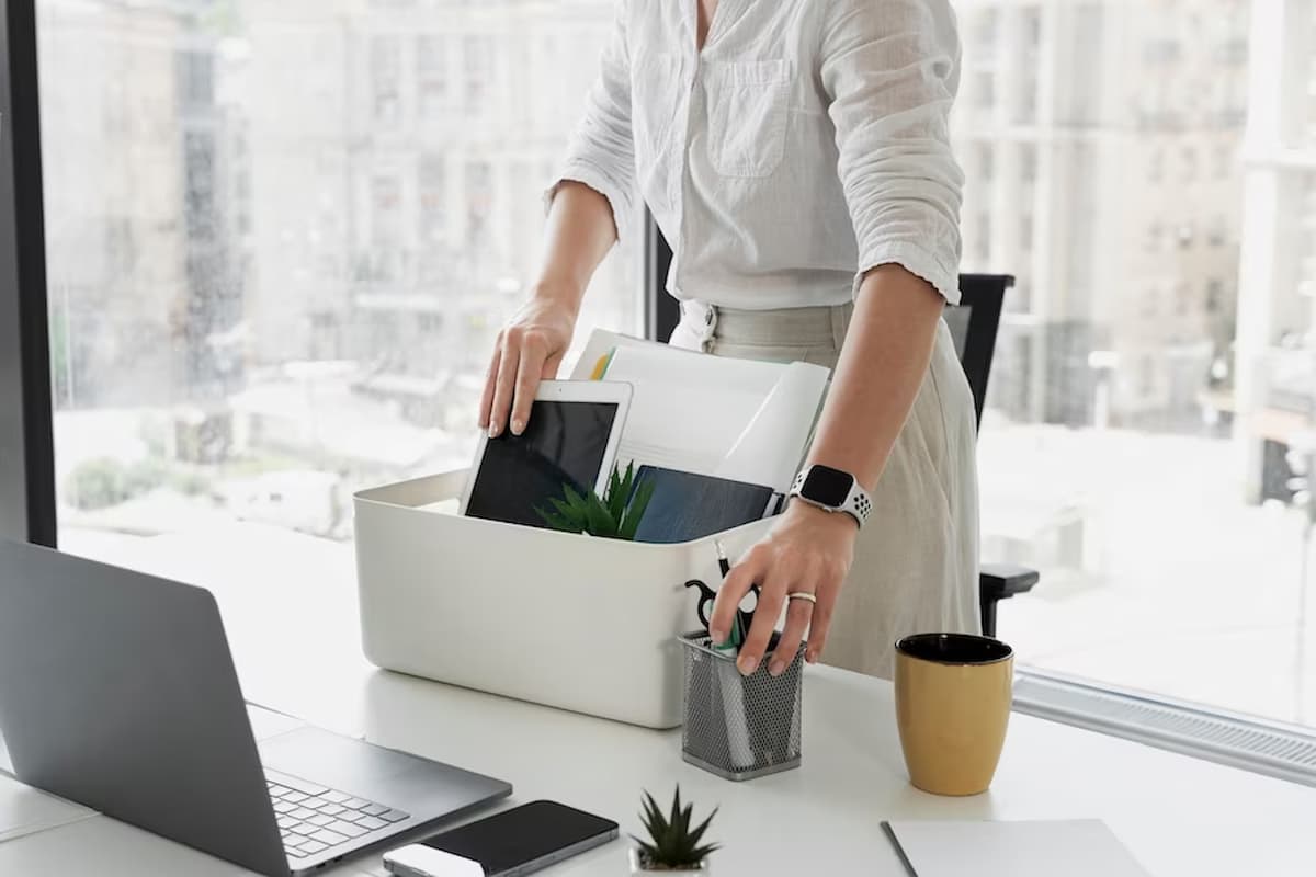 Imagem de uma mulher segurando uma caixa com seus pertences de escritório após demissão.