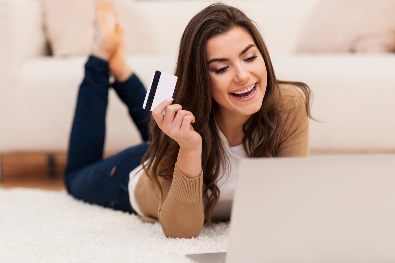 Mulher fazendo compras via internet segurando um cartão de crédito.