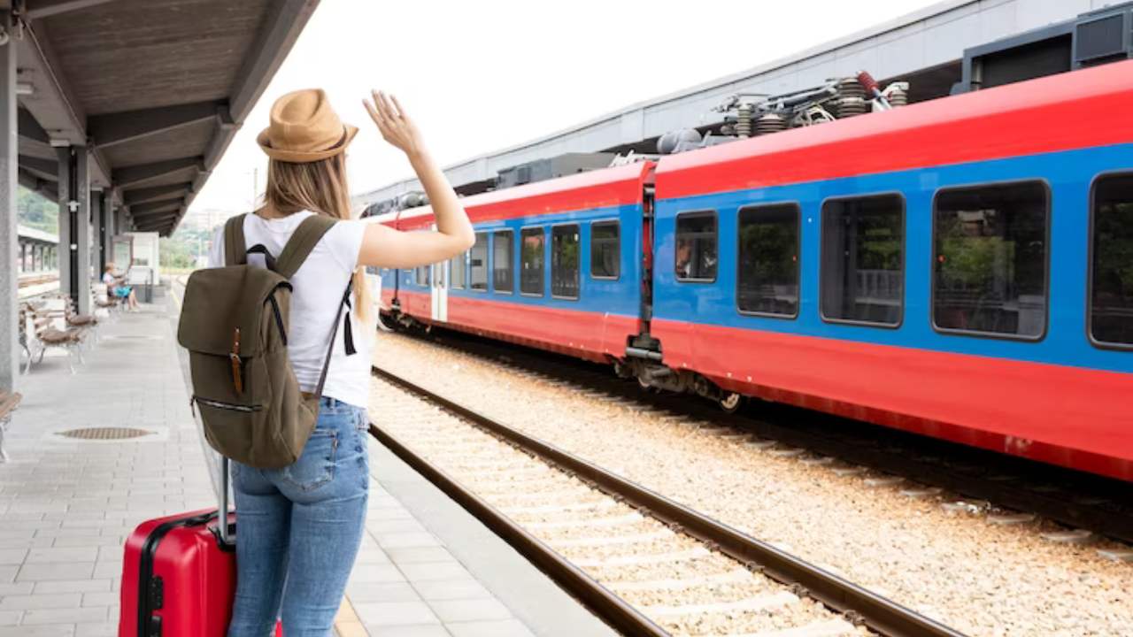 Mulher segurando uma mala vermelha acena para trem turístico.