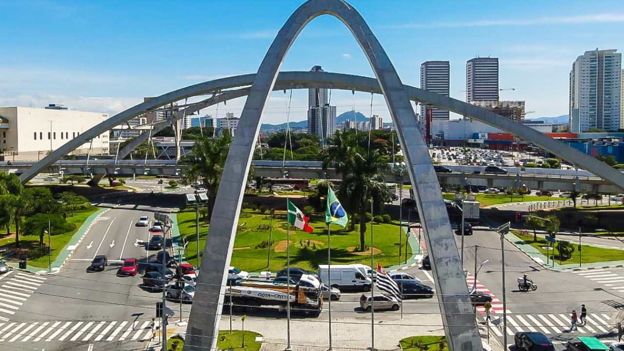 Vista aérea do centro da cidade de Osasco, onde vê-se o Monumento da cidade, vários carros e as bandeiras do Brasil, do estado e da cidade.