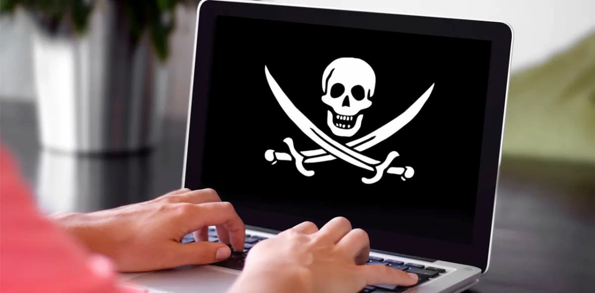 Pessoa usando notebook com símbolo pirata na tela: uma caveira branca com duas espadas cruzadas abaixo em um fundo preto.
