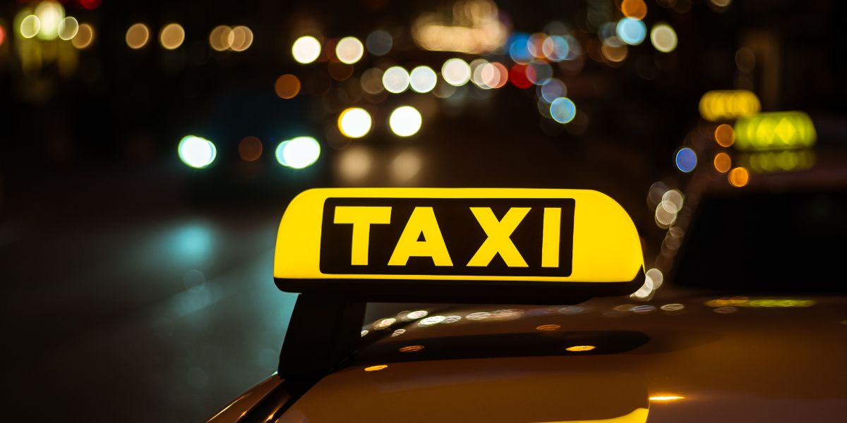 Placa amarela e preta de táxi colocada em cima de um carro à noite.