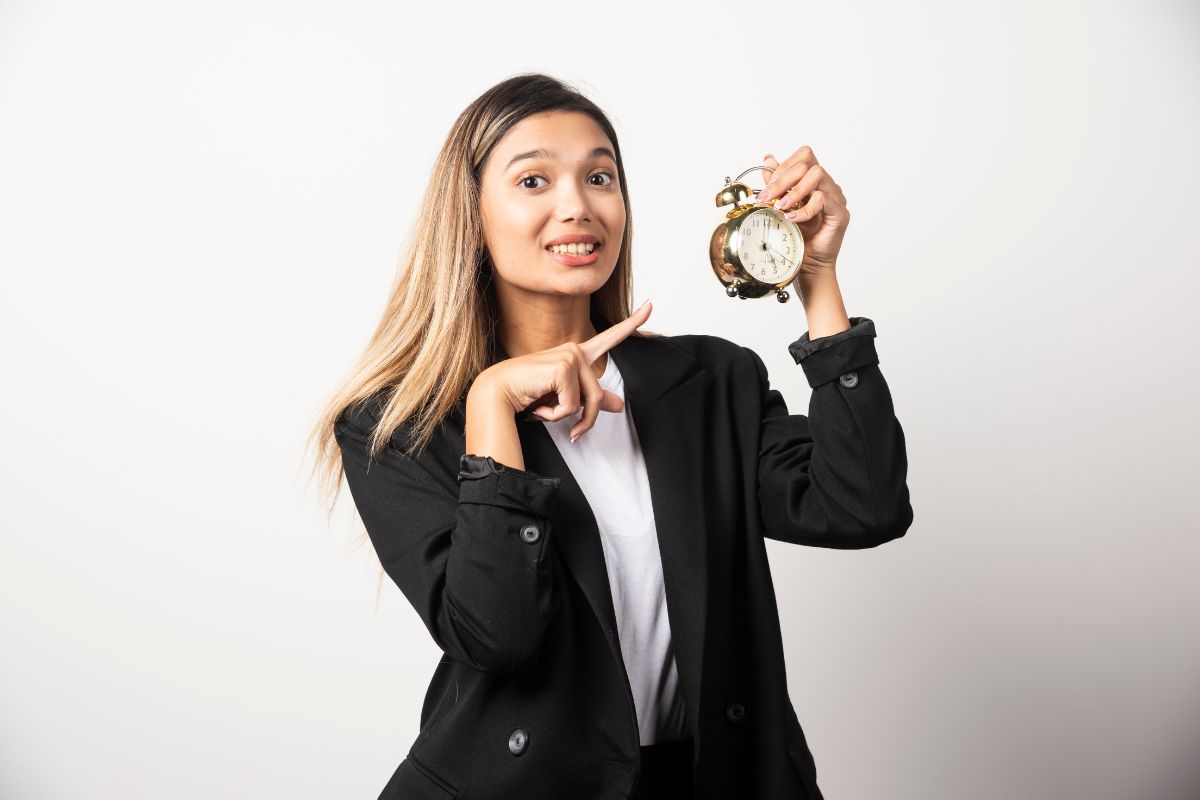 Emprego temporário. Mulher de negócios, usando terno, está apontando com a mão direita para um relógio que está em sua mão direita em alusão a emprego temporário.